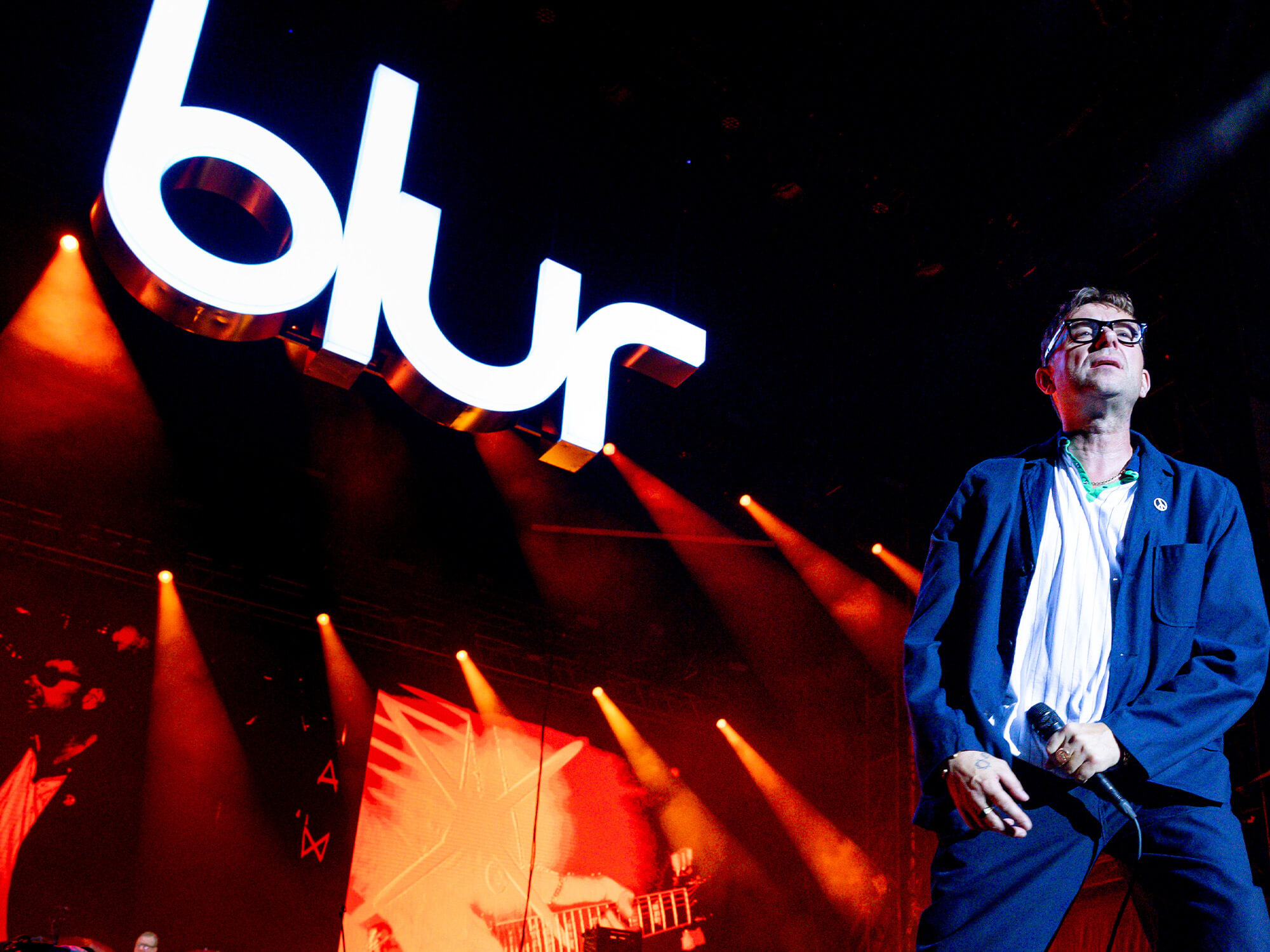 Damon Albarn on stage with Blur logo in the background