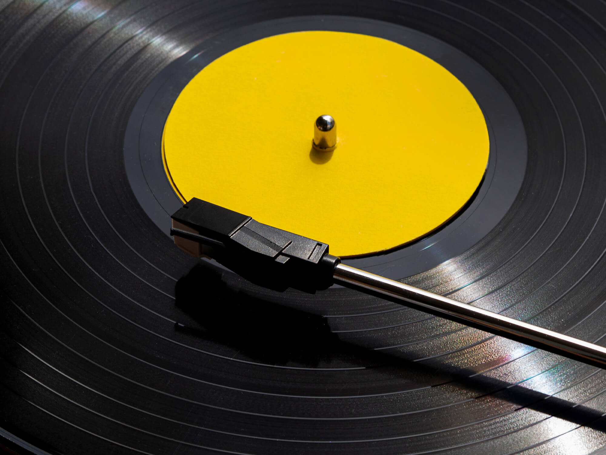 A close up of a vinyl record under a needle. The centre of the record is bright yellow, like the colour of a rubber duck.
